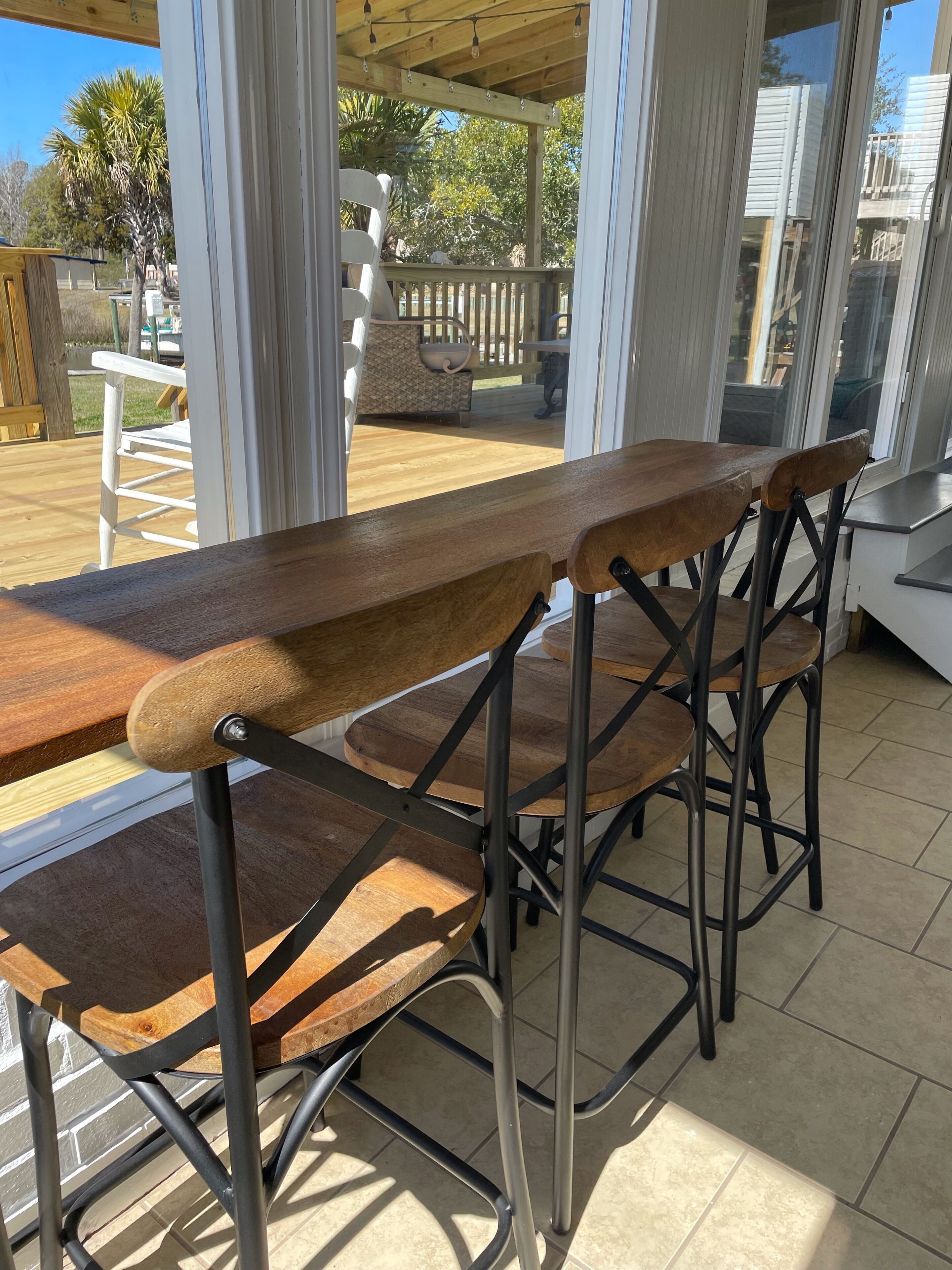 A wooden bar stool set in a covered outdoor area with a view of a wooden deck and a white fence.