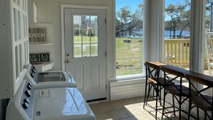 A room with a white door, a fish-shaped decoration, a view of a lake, and a wooden table with chairs.