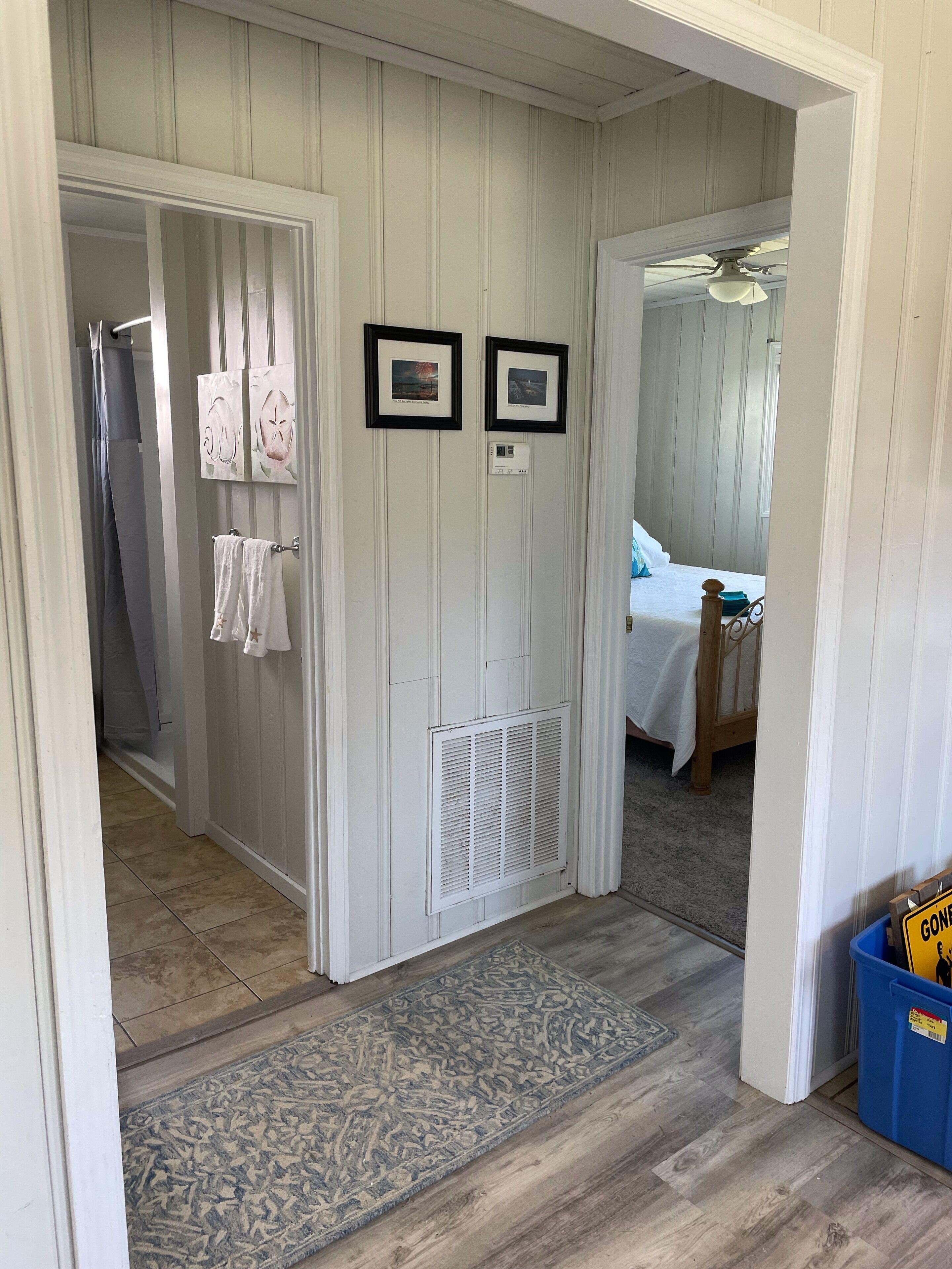 A hallway with a door leading to a bedroom, a radiator, and a blue trash bin with a 'Gone' sign.