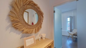A room with a round mirror, a framed sign, a small white vase, and a wooden console table.