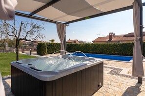 Uma banheira de hidromassagem com vista para uma piscina e um terraço coberto.