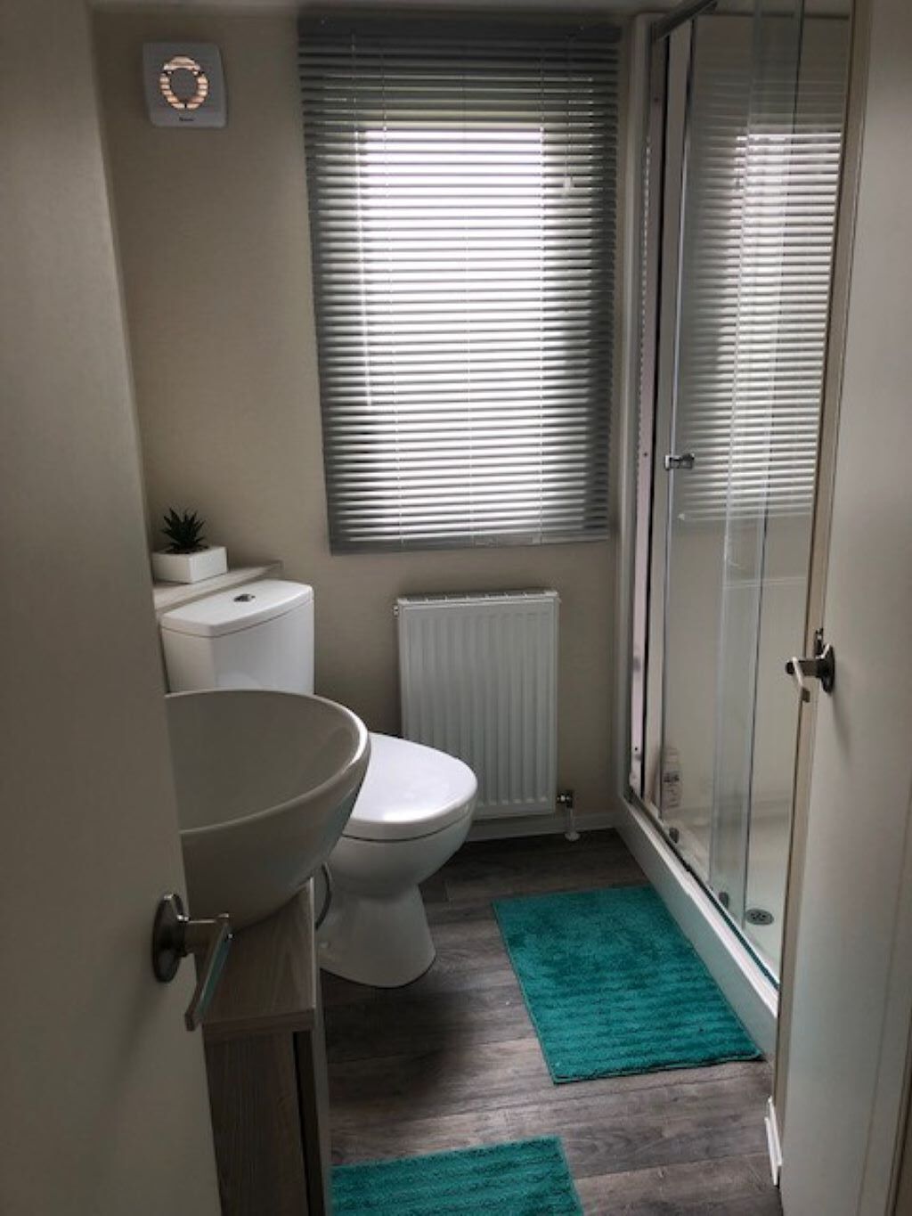 A small bathroom with a toilet, sink, and a window with blinds.