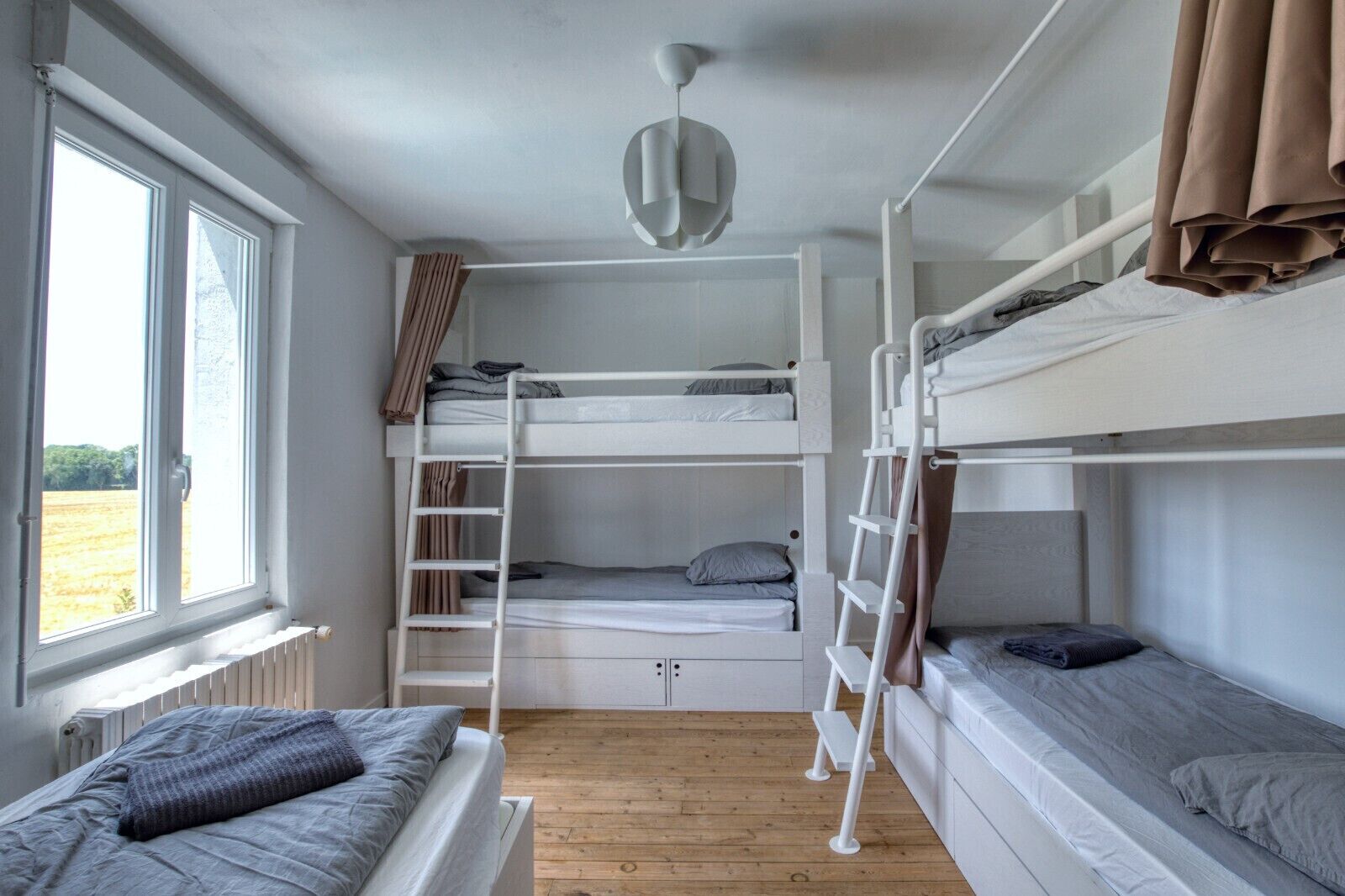 Ein Schlafraum mit Etagenbetten, einer Leiter, einem Fenster mit Vorhängen und einer Heizung.