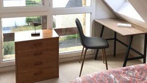 Ein Schlafzimmer mit schrägen Wänden, einer Holzkommode, einem Stuhl, einem Schreibtisch und einem Bett.