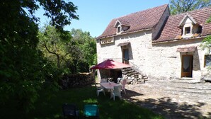 A stone building with a red-tiled roof, a patio with a table and chairs, and a stone wall. - Country house with lots of outdoor space (Beauregard)