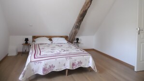 A bedroom with a sloped ceiling, a bed with a floral bedspread, two bedside tables with lamps, and a geometric pendant light. - Country house with lots of outdoor space (Beauregard)