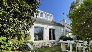 Een huis met een grote schuifdeur, een terras met buitenmeubilair en een tuin met verschillende planten en bloemen.