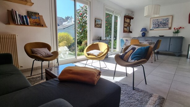 Een moderne woonkamer met een bank, twee fauteuils, een salontafel en een eethoek met een tafel en stoelen.