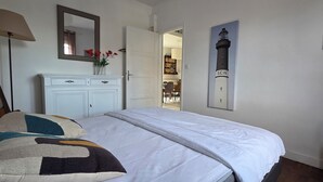 Een slaapkamer met een bed, een kaptafel, een lamp, een gitaar en een deur naar een andere kamer.