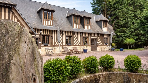A traditional half-timbered building with a gravel courtyard, outdoor seating, and a stone wall. - Le Pressoir - Domaine de Geffosses (PONT L EVEQUE)