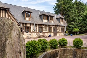 Un bâtiment traditionnel à colombages, doté d’une cour en gravier, d’un espace extérieur aménagé pour s’asseoir et d’un mur en pierre.
