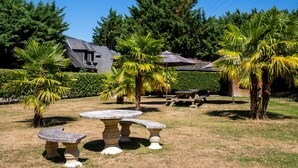 A stone table and benches in a grassy area with a house and trees in the background. - Le Pressoir - Domaine de Geffosses (PONT L EVEQUE)
