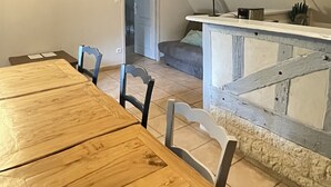 A dining area with a wooden table and chairs, a kitchen area with a counter and appliances, and a staircase leading to an upper level. - Le Pressoir - Domaine de Geffosses (PONT L EVEQUE)