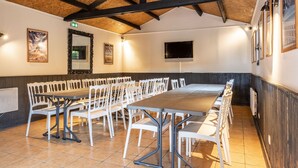 A conference room with a long table and white chairs, wooden beams on the ceiling, and framed pictures on the walls. - Le Pressoir - Domaine de Geffosses (PONT L EVEQUE)