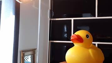 Un patito de goma amarillo sobre una mesa de madera con un muro de azulejos negros al fondo.