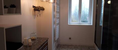 A bathroom with a patterned floor, a window, a shower, and a mirror.