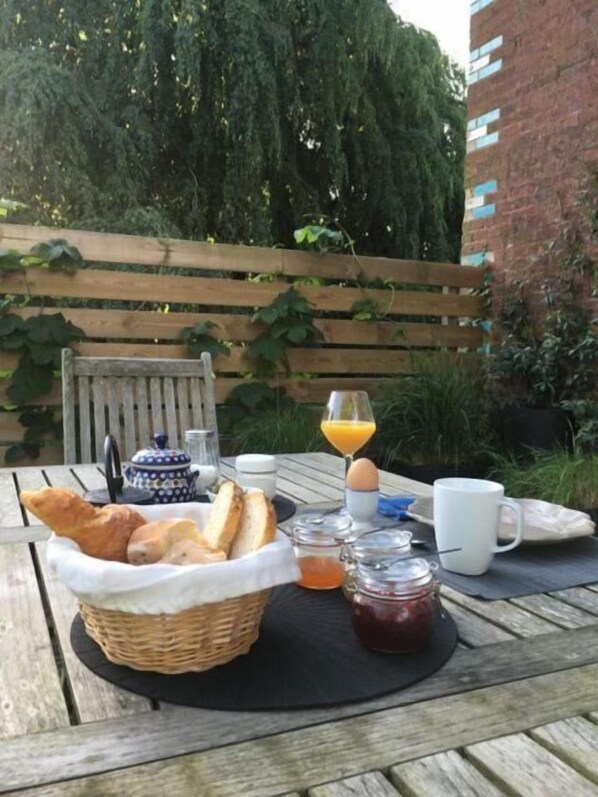 Un desayuno servido en una mesa de madera al aire libre, con pan, huevos, jugo y salsas.