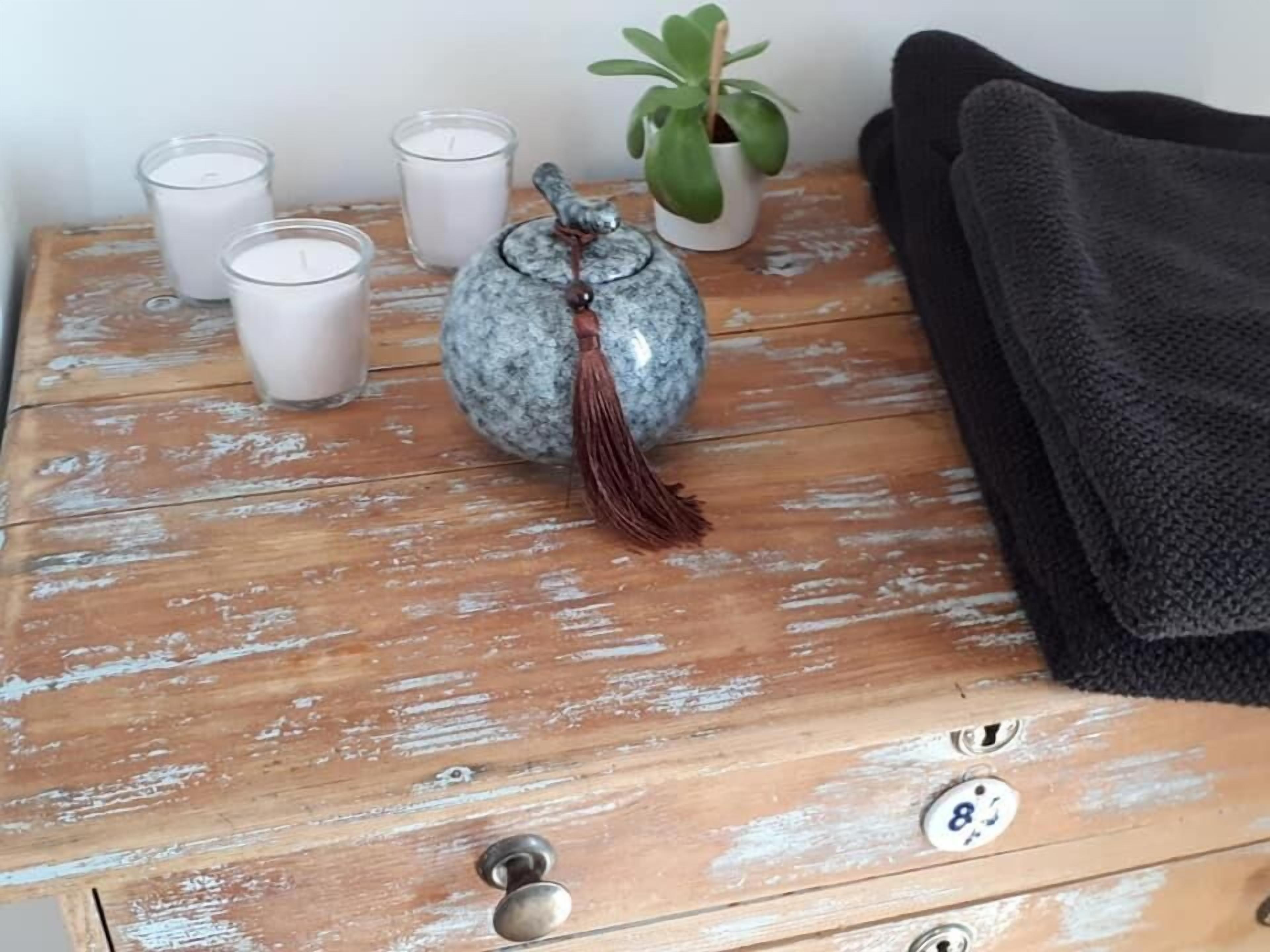 A wooden dresser with a rustic finish, a potted plant, three candles, a decorative stone jar, and a black towel.