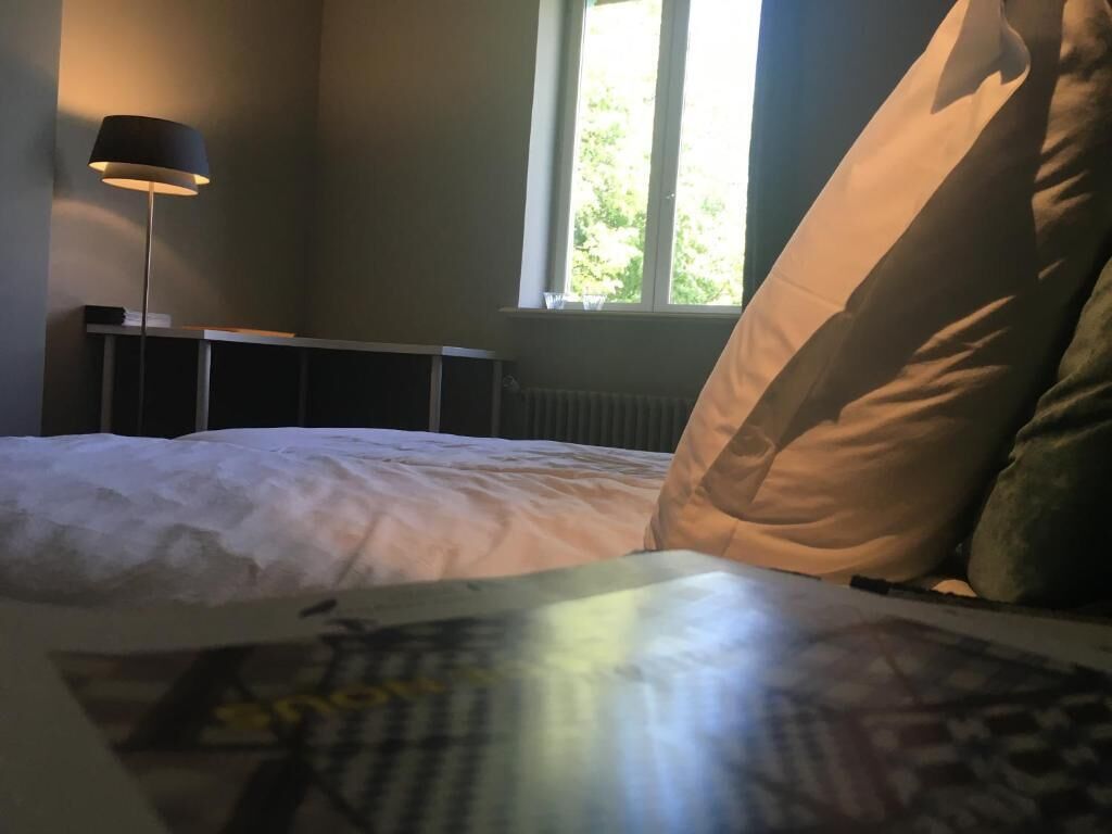 A bedroom with a bed, pillows, a lamp, and a window.