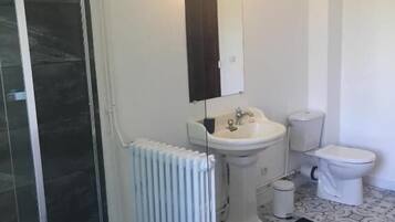 Un baño con cabina de ducha de vidrio, lavabo pedestal, inodoro y radiador.