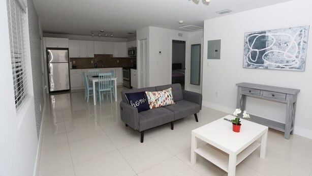 Um apartamento moderno com um sofá cinzento, uma mesa de centro branca e uma cozinha ao fundo.