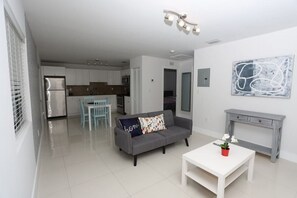 Un appartement moderne avec un canapé gris, une table basse blanche et une cuisine en arrière-plan.