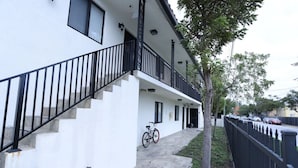 Um edifício de dois andares com fachada branca, guarda-corpo preto na escadaria e uma bicicleta estacionada em frente.