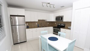 Cozinha moderna com armários brancos, eletrodomésticos de aço inoxidável e área de jantar com mesa branca e cadeiras azuis.