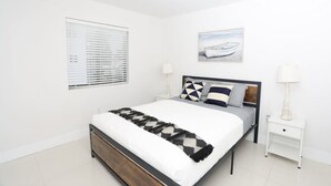 Um quarto moderno com uma cama grande, uma mesa de cabeceira, uma janela com persianas e um lustre no teto.