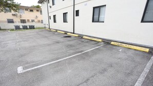 Um estacionamento com vagas demarcadas e um edifício com várias janelas e uma porta.