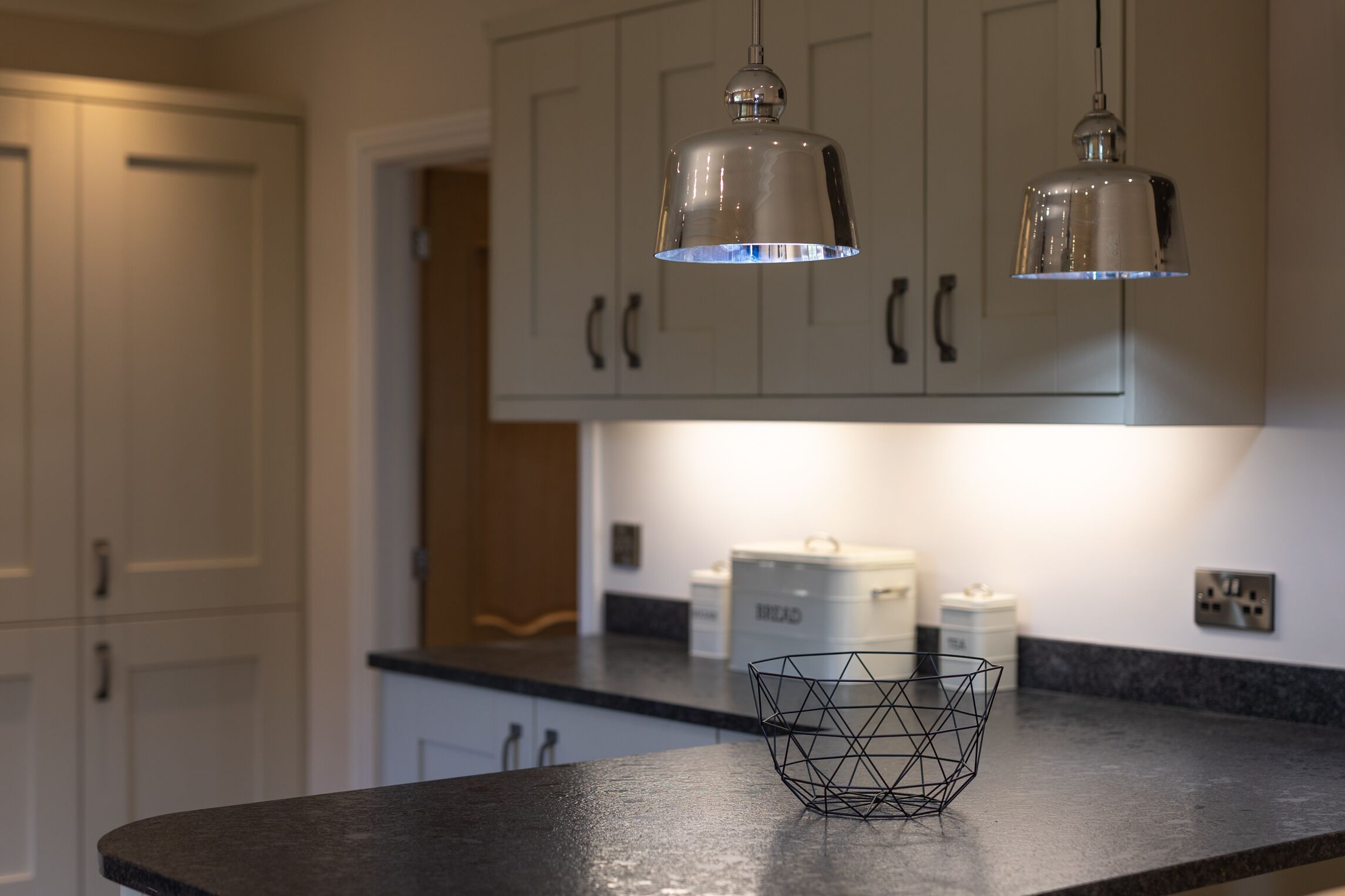 Une cuisine avec des armoires blanches, un plan de travail noir et deux luminaires suspendus.