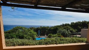 A view from a covered outdoor area with a pool and lush greenery, overlooking a body of water.