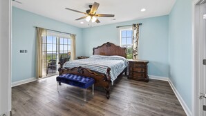 A bedroom with a large bed, a ceiling fan, and a view through a sliding glass door.