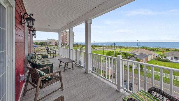 A covered porch with wicker furniture, a view of the ocean, and a white fence.