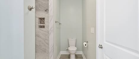 A bathroom with a toilet, shower, and tiled floor.