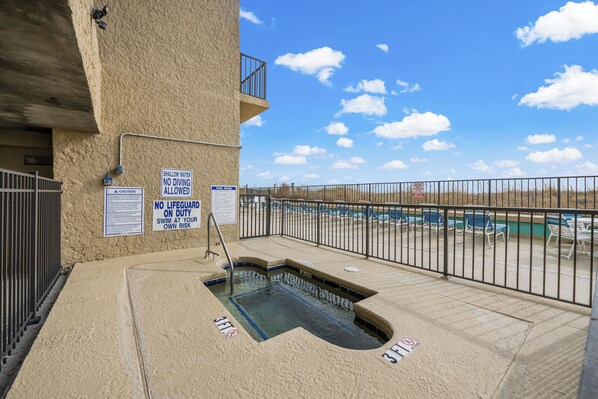 Un área de piscina pequeña con señales de seguridad, un suelo de hormigón y vista a un estacionamiento.