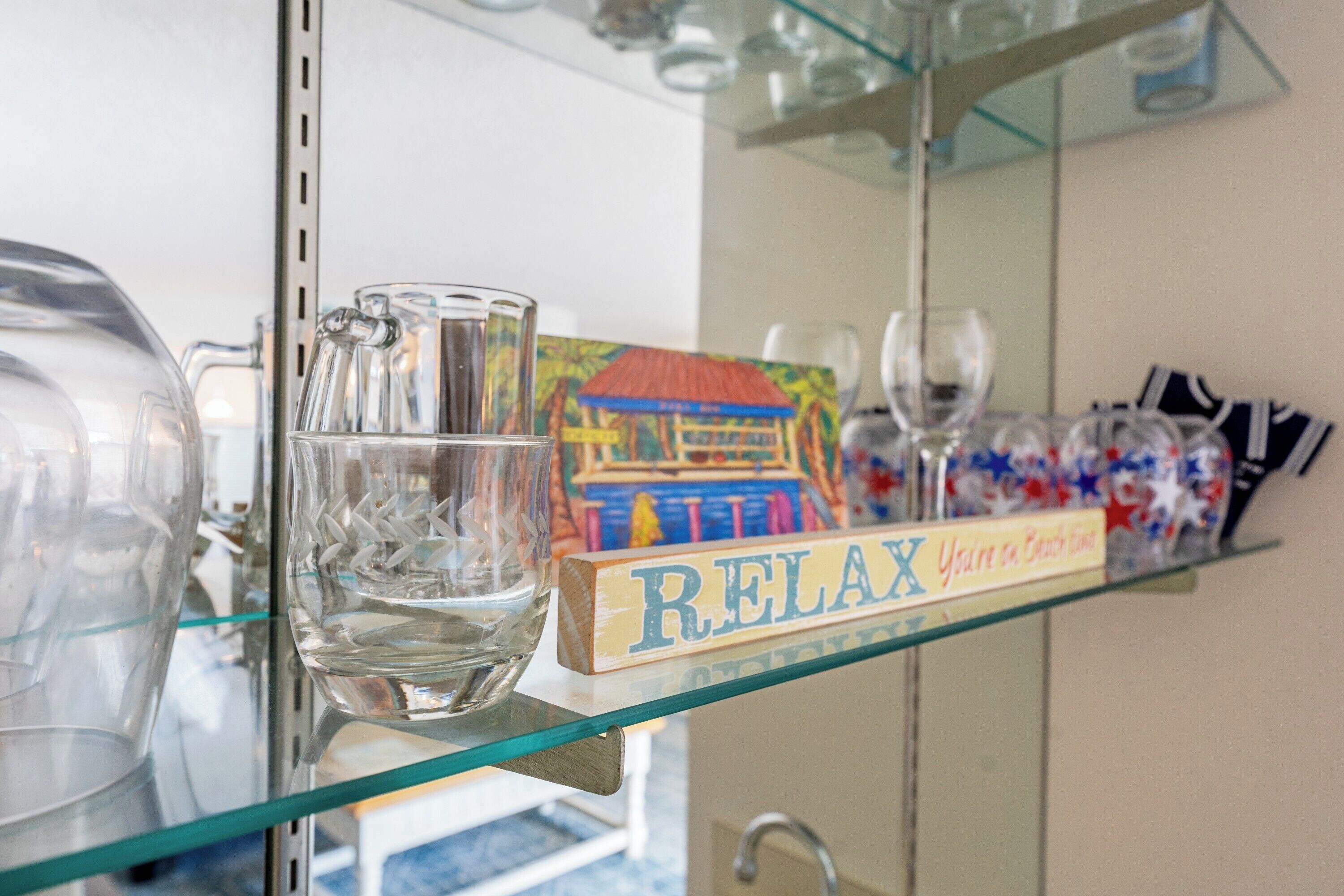 A glass shelf with a 'RELAX' sign, a decorative box, and a clear glass pitcher.