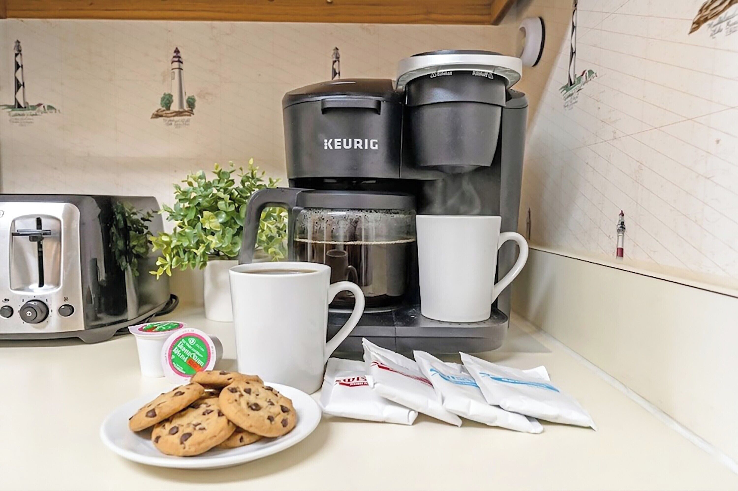 A kitchen with a Keurig coffee maker, a toaster, a plate of cookies, a mug, and a small plant.