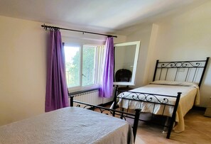 Ein Schlafzimmer mit einem Einzelbett, einem Fenster mit violetten Vorhängen, einem Heizkörper und einem kleinen Tisch.