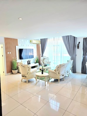 A modern living room with a flat-screen TV, white armchairs, a coffee table, and a large window with curtains. - VIP 3BR Deluxe in Cantonments (Accra)