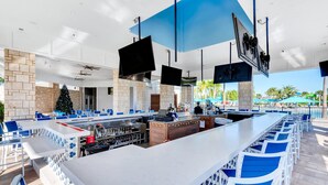 A modern outdoor bar area with multiple seating arrangements, a central bar counter, and a large screen.