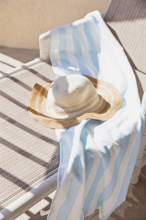 Une chaise longue pour bronzer, avec une serviette à rayures et un chapeau de paille.