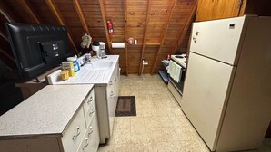Eine kleine Küche mit Holzbalkendecke, einem Kühlschrank, einem Herd, einer Spüle und einer Mikrowelle.
