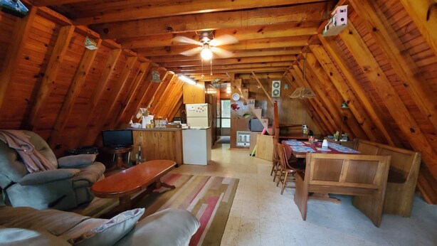 Ein gemütlicher Dachbodenraum mit Holzbalkendecke, Deckenventilator, Küchenzeile, Esstisch mit Stühlen und einer Couch.
