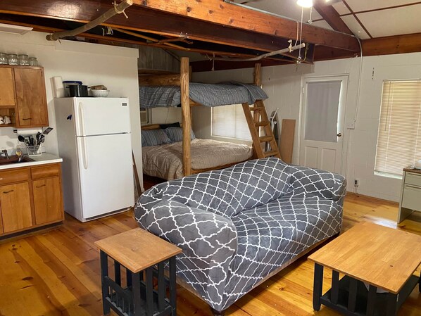 Een knus, rustiek kamertje met een stapelbed, een kitchenette met een koelkast en een klein houten tafeltje.