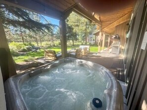 A hot tub in a covered outdoor area with a view of a garden and a house in the background.
