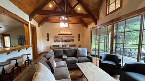 A spacious living area with a large sectional sofa, a wooden coffee table, and a dining table with chairs. There is a large window providing a view of the outdoors. - Crosswater Luxury Retreat with Access to Exclusive Golf (Sunriver)