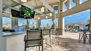 Een terras met een bar, een televisiescherm, verschillende zithoeken en uitzicht op het zwembad en de gebouwen van het resort.