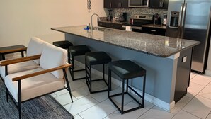 Een moderne keuken met donkerhouten kastjes, een roestvrijstalen koelkast, een magnetron en een granieten kookeiland met barkrukken.