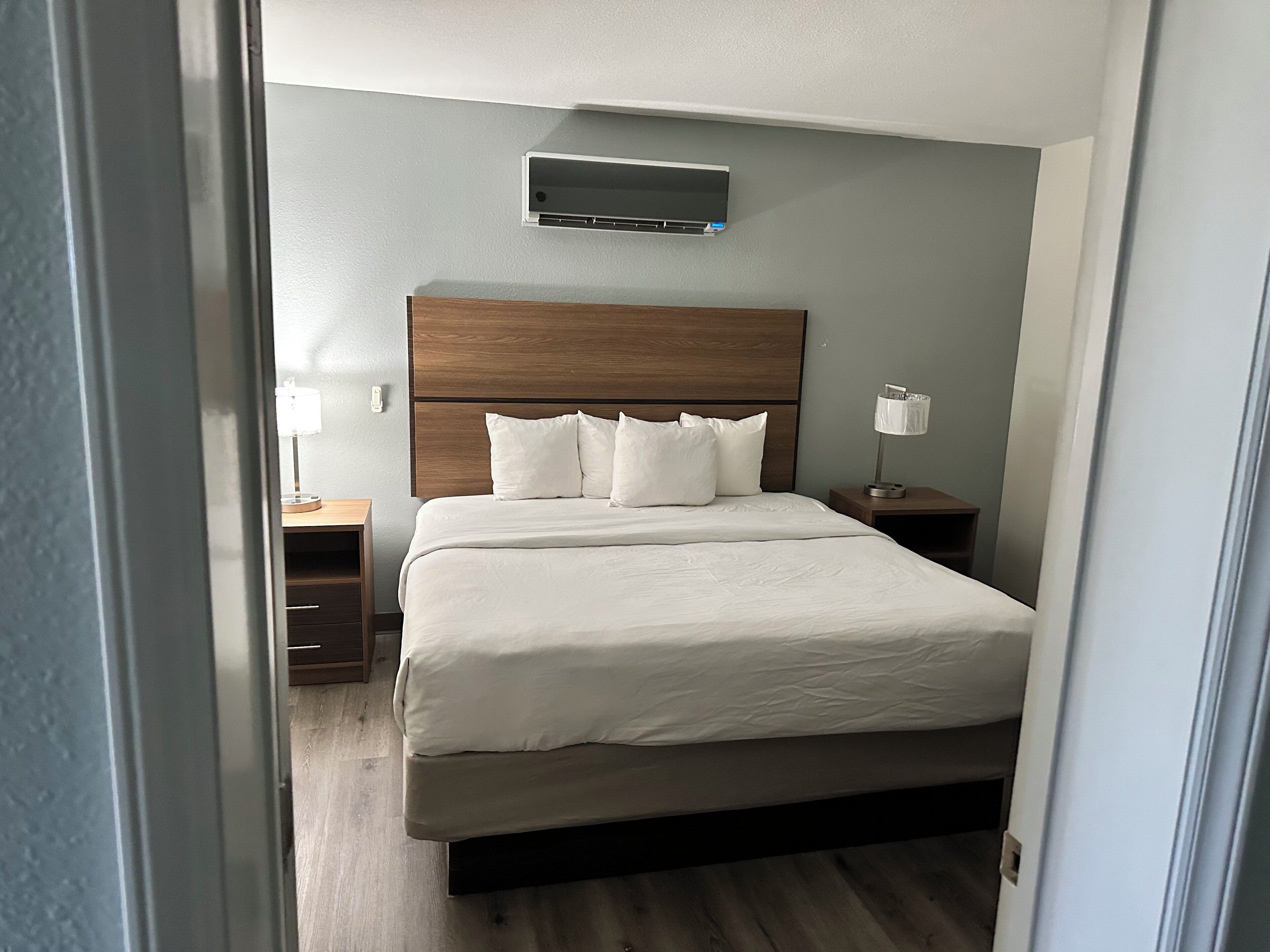 Habitació d'hotel amb un llit, una tauleta de nit, una làmpada i un aire condicionat fixat a la paret.